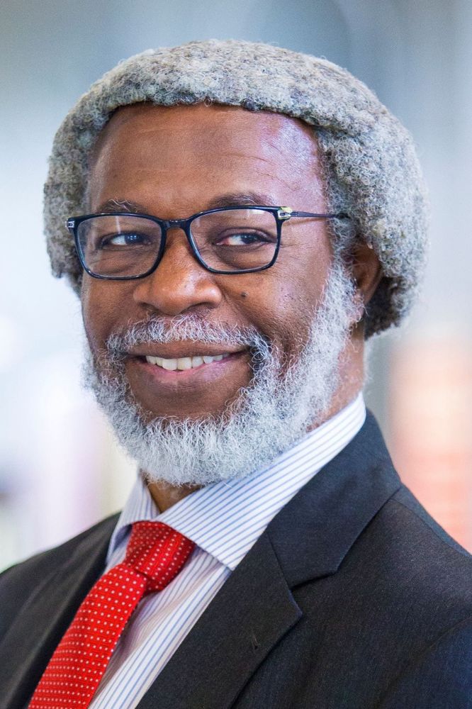 Professional headshot of a smiling man with glasses and a beard in a suit with a red tie