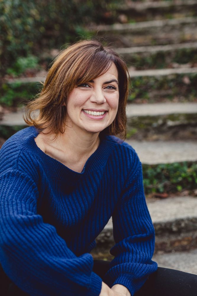 Smiling woman with shoulder-length hair and a blue sweater seated outdoors